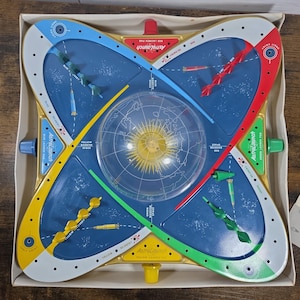 May include: A vintage AstroLaunch board game in its original box. The game board is blue, yellow, red, and green with a clear plastic globe in the center. The game includes small plastic rockets and launch pads. The box is white.