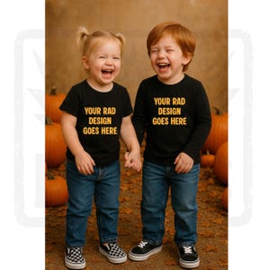 May include: Two young children, a girl and a boy, are holding hands and laughing. They are wearing matching black shirts with the text "YOUR RAD DESIGN GOES HERE" in gold. The girl wears a short-sleeved shirt, and the boy wears a long-sleeved shirt. Both are wearing blue jeans and sneakers.