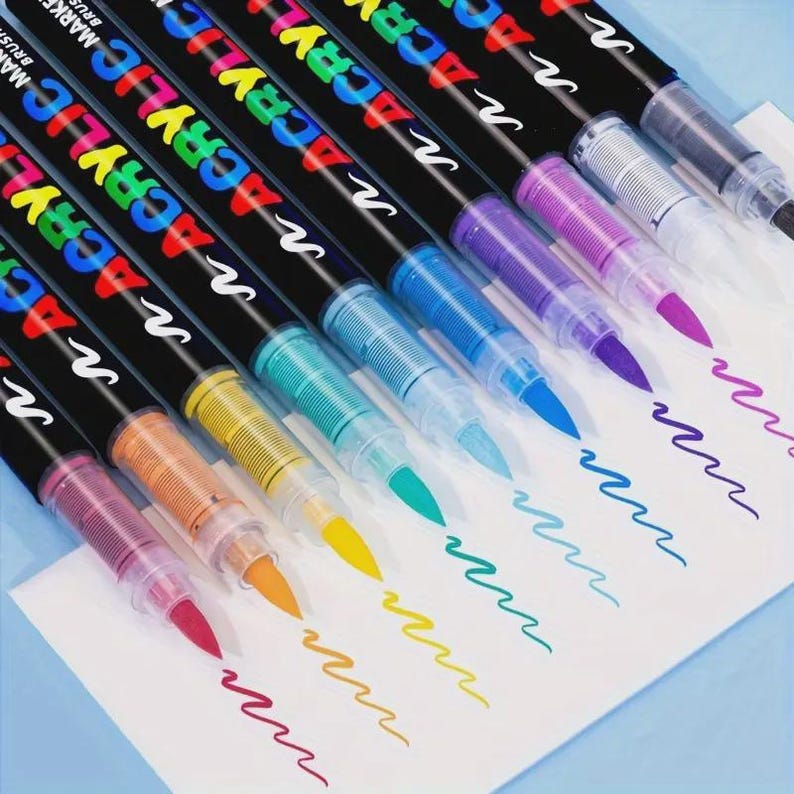May include: A collection of colorful acrylic brush pens with black barrels. The pens are arranged diagonally, showcasing their vibrant ink colors: pink, orange, yellow, green, blue, purple, and black. Each pen has the word "ACRYLIC" in rainbow colors.