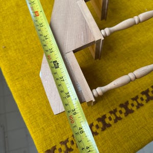 May include: A light-colored wooden shelf with two tiers and turned legs. A yellow measuring tape shows the shelf is approximately 38 inches long. The shelf is on a yellow and brown patterned surface.