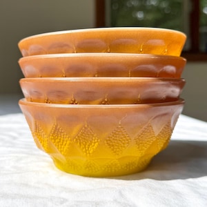 May include: A stack of four vintage amber-colored glass bowls. The bowls have a textured diamond pattern on the lower half, transitioning from yellow to amber. The rims have a beaded design.