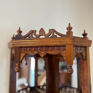 May include: A brown wooden corner shelf featuring an intricate fretwork gallery top with decorative finials. The structure includes a scalloped apron with vertical fluting and mirrored panels set into the back walls of the corner unit.