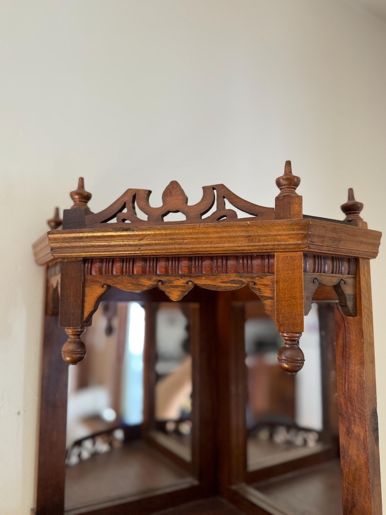 May include: A brown wooden corner shelf featuring an intricate fretwork gallery top with decorative finials. The structure includes a scalloped apron with vertical fluting and mirrored panels set into the back walls of the corner unit.