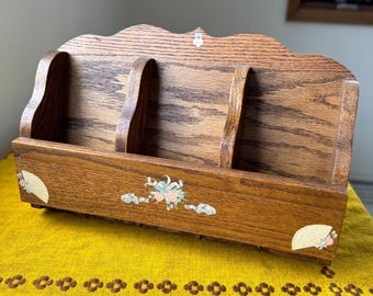 May include: A vintage wooden desk organizer with three compartments. The organizer is made of light brown wood and features decorative floral and fan-shaped accents. The top edge has a decorative scalloped design.