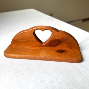 May include: A wooden shelf with a heart-shaped cutout in the center. The shelf is made of light brown wood and has a curved top. The shelf is designed to be mounted on a wall.
