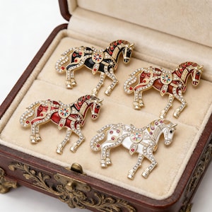 May include: A collection of five horse-shaped brooches in a wooden jewelry box. The brooches feature gold-tone metal, colorful enamel, and sparkling rhinestones. Each brooch has a unique color scheme, including black, red, and white.