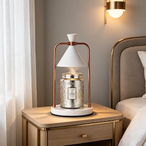 May include: A decorative silver glass jar with a floral pattern sits on a white base, topped with a white conical shade and copper-colored metal frame. The jar is emitting steam, suggesting it is an aromatherapy diffuser or candle warmer.