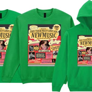 May include: Green t-shirts, a sweatshirt, and a hoodie featuring a colorful graphic. The graphic reads "THIS TOUR MAY CONTAIN NEW MUSIC" with images of a woman, musical notes, and the word "MUSICAL".