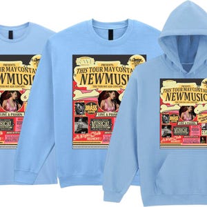 May include: Light blue t-shirts and a hoodie featuring a colorful graphic. The graphic reads "THIS TOUR MAY CONTAIN NEW MUSIC" with images of musicians and the words "BRASS" and "MUSICAL".