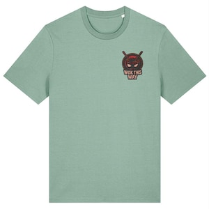 May include: A light green t-shirt with a crew neck. The shirt features a small graphic on the chest of a ninja mask with crossed chopsticks and the text "WOK THIS WAY" in a red and brown color scheme.