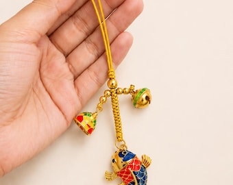 May include: A gold-toned decorative charm featuring a koi fish pendant with blue, red, and gold enamel detailing. The charm hangs from a yellow braided cord and includes two small, colorful metal bells attached to the upper section of the cord.