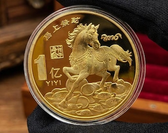 May include: A gold coin featuring a detailed relief of a horse with ornate tack. The coin has Chinese characters and the number "1" with "YIYI" below. The coin is encased in a clear protective case.