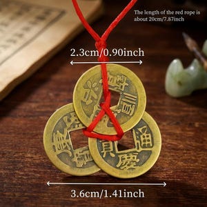 May include: Three antique bronze Chinese coins strung on a red cord. The coins are 1.41 inches wide and 0.90 inches in diameter. The red cord is 7.87 inches long. The coins have Chinese characters.