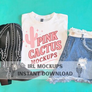 May include: A white t-shirt with a pink cactus design and the text "Pink Cactus Mockups." The image also features a pair of denim shorts and a black cowboy boot. The background is a solid teal colour.