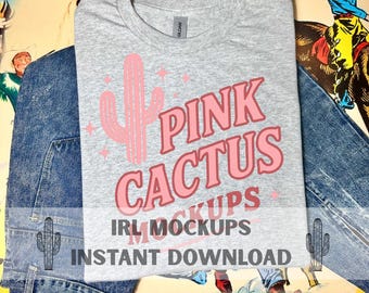 May include: A grey t-shirt featuring a pink cactus graphic and the words "PINK CACTUS" in a retro style. The t-shirt is folded on top of blue denim jeans. The text "IRL MOCKUPS" and "INSTANT DOWNLOAD" are also visible.
