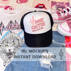 May include: A black and white trucker hat with the text "PINK CACTUS MOCKUPS" in pink, a white t-shirt with a graphic design, and a pair of pink sneakers. The image also includes a pair of blue denim shorts with distressed details.