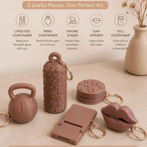 May include: A keychain kit featuring five brown items: a kettlebell-shaped container with the letter J, a floral-patterned cylindrical container, a flat circular container, a rectangular folding phone stand, and a lip-shaped container.