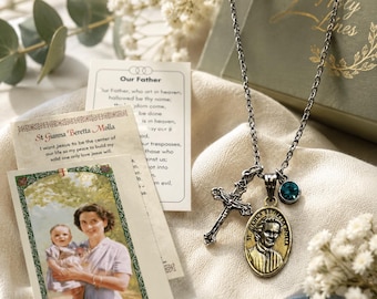 May include: A silver-toned metal chain necklace featuring a crucifix pendant, an oval-shaped medal depicting St. Gianna Beretta Molla, and a small round teal crystal charm, accompanied by a prayer card and a card with the Our Father prayer.