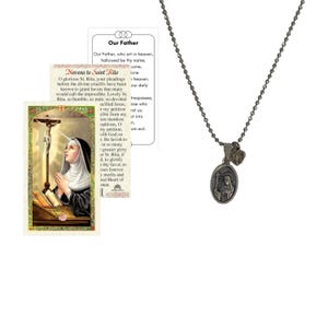 May include: A silver-toned necklace with a pendant featuring an image of a saint, accompanied by prayer cards. The pendant is oval-shaped and hangs from a ball chain. The prayer cards have text and images.