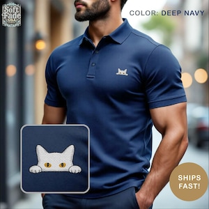 May include: Deep navy blue polo shirt with a small embroidered cat design. The shirt has a classic collar and button closure. The image also includes a close-up of the cat design and the text "COLOR: DEEP NAVY".