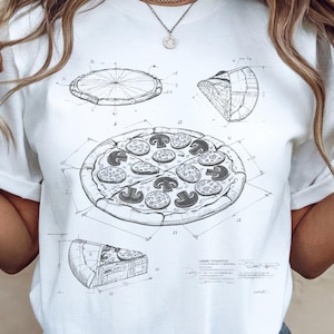 May include: White t-shirt featuring a detailed blueprint-style illustration of a pizza, including a whole pizza, a slice, and a crust. The pizza has mushroom and pepperoni toppings. The design is in black and white.