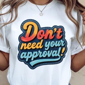 Può includere: T-shirt bianco con una grafica colorata che recita "Don't need your approval!". Il testo è in stile retrò, con un bordo in denim. Un capo casual per l'uso quotidiano.