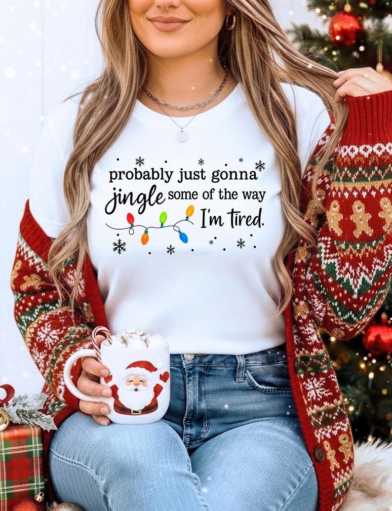 A woman wearing a white t-shirt with a humorous Christmas-themed text and a red and green sweater, holding a mug with a Santa Claus design.