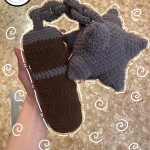 May include: Crocheted brown and gray bottle stopper with a gray chain and a gray starfish. The bottle stopper is cylindrical with a gray band near the top. The starfish is five-pointed and plush.