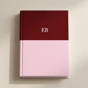 May include: A hardcover journal with a two-tone design. The top half is a deep burgundy, and the bottom half is a soft pink. The initials "ER" are printed in white on the burgundy section.