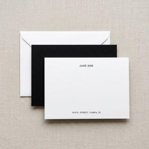 May include: A stationery set featuring a white envelope, a black card, and a white card. The white card has the name "JANE DOE" and address "1010 E. STREET, TAMPA, FL" printed in black.