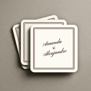 Puede incluir: Una pila de tres posavasos cuadrados de color blanco roto con esquinas redondeadas. Cada posavasos presenta un borde de doble línea marrón oscuro y el texto impreso Amanda & Alenjandro en cursiva marrón oscuro centrado en la superficie.