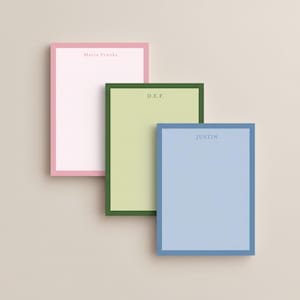 May include: Three rectangular notepads in pastel colors: pink, green, and blue. Each notepad has a contrasting border and personalized text at the top: "Maria Franks", "D.E.F.", and "JUSTIN". The notepads are arranged in a slightly overlapping manner.