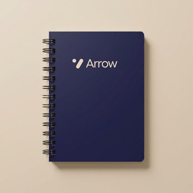 Clean white spiral notebook mockup featuring a centered blue geometric logo and “Custom Design Here” text. Ideal for businesses creating branded office supplies, promotional event notebooks, and personalized company planners. Perfect for entrepreneurs, startups, and corporate teams seeking cohesive branding materials. Sleek, modern spiral notebook for professional use, journaling, and team appreciation gifts.