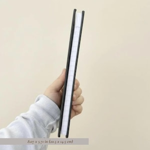 Side profile mockup of a slim personalized hardcover notebook held in hand against a soft neutral background, showing journal thickness, lined page count, and sleek premium binding. Minimalist stationery product photography featuring a modern monogram notebook, luxury office journal, professional note taking book, custom planner cover view, elegant desk accessory, personalized writing journal, premium paper goods, giftable notebook design, and high end stationery for office organization.