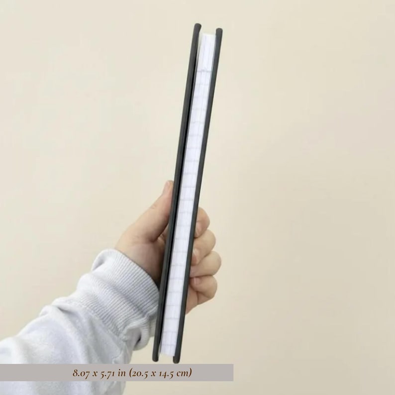 Side profile mockup of a slim personalized hardcover notebook held in hand against a soft neutral background, showing journal thickness, lined page count, and sleek premium binding. Minimalist stationery product photography featuring a modern monogram notebook, luxury office journal, professional note taking book, custom planner cover view, elegant desk accessory, personalized writing journal, premium paper goods, giftable notebook design, and high end stationery for office organization.