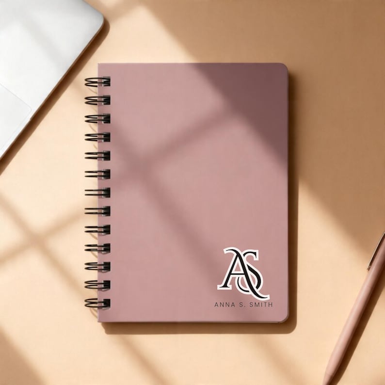 Professional brown spiral notebook mockup featuring a custom gold logo on the front cover beside open lined pages. Perfect for business branding, corporate stationery, or executive office gifts. Personalized business journal ideal for professional note-taking, client meetings, and promotional branding. Durable wire-bound planner for offices, companies, or entrepreneurs looking for custom logo notebooks.