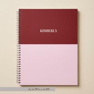 May include: A spiral-bound notebook featuring a two-tone cover with a dark red top half and a light pink bottom half. The name KIMBERLY is printed in white in the center of the red section. The notebook measures 8.5 inches wide by 11 inches high.