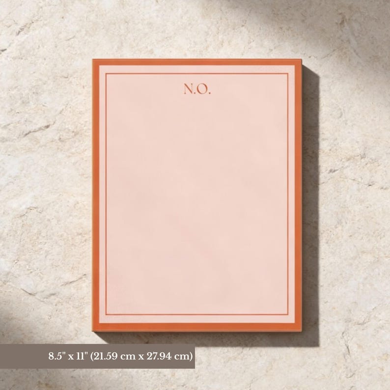 May include: A rectangular notepad with a peach-colored interior and a burnt orange border. The upper left corner features the initials "N.O." in a matching burnt orange color. The notepad is set against a light-colored, textured background.