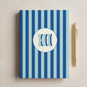 Blue and light blue striped personalized notebook with monogrammed initials on the cover beside a decorative branch. Elegant hardcover journal with perforated lined pages for daily writing, school, or office notes. Aesthetic blue stripe design perfect for journaling, business planning, or gift-giving. Custom name notebook ideal for professionals, students, and lovers of unique stationery.