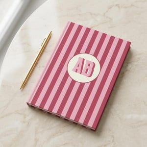 Burgundy and pink striped personalized notebook with custom initials on the cover. Elegant monogrammed journal featuring perforated lined pages for writing, planning, or note-taking. Aesthetic hardcover diary perfect for students, professionals, and gift-giving. Custom name notebook for journaling, office, or school use. Stylish pink stripe stationery gift for teachers, coworkers, or friends who love personalized and chic writing essentials.