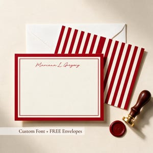 Personalized red bordered notecard with custom name in script font, paired with a red and white striped envelope, wax seal stamp, and red wax seal. personalized red bordered notecard, custom name stationery set, red and white striped envelope, wax seal stationery flat lay, elegant script monogram notecard