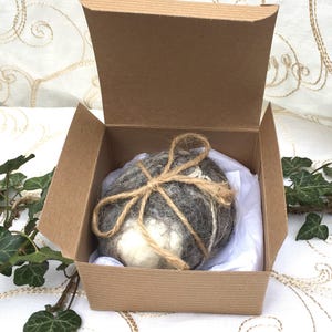 May include: A round, white and grey felted ball wrapped in twine and placed in a brown cardboard box with white tissue paper.