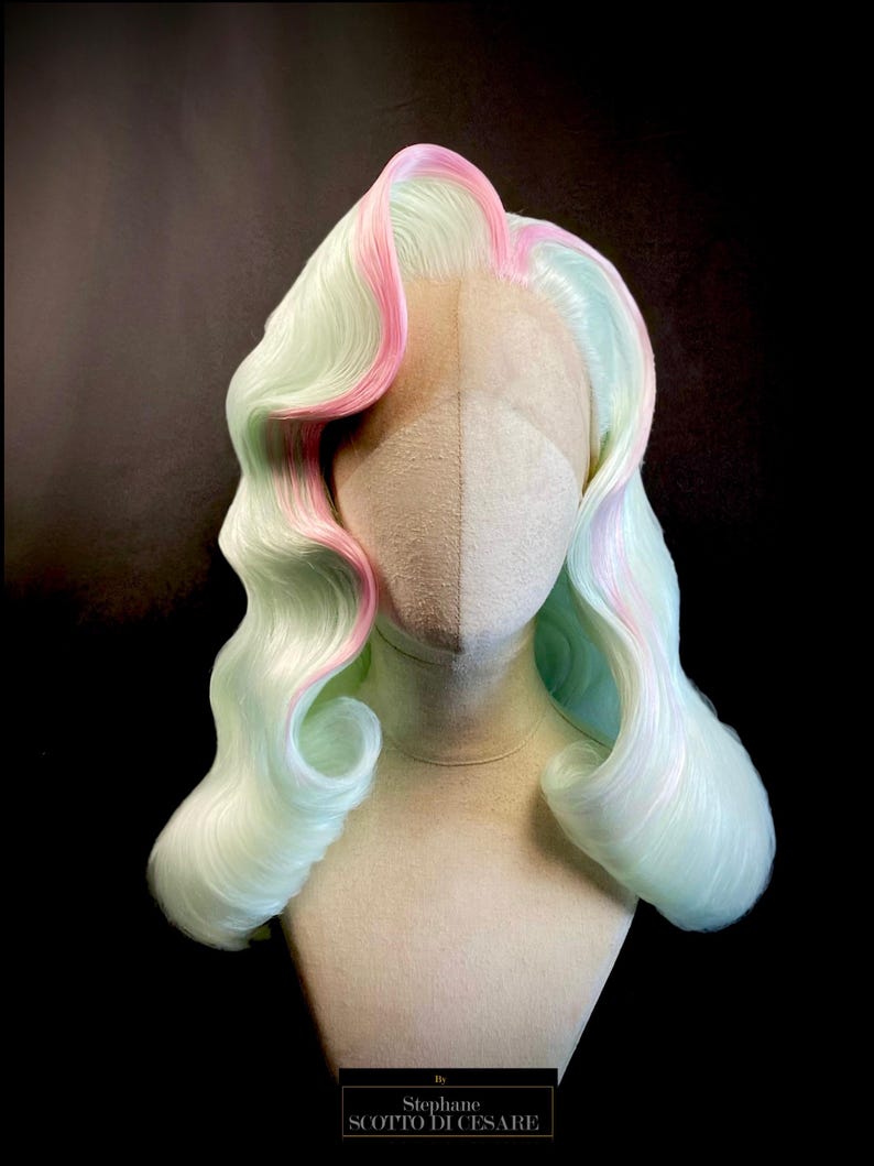 Puede incluir: Peluca de color pastel con base verde claro y mechas rosas, peinada con rizos largos y ondulados. La peluca se exhibe sobre una cabeza de maniqu&iacute; sobre un fondo oscuro. La peluca tiene una parte delantera de encaje y est&aacute; etiquetada "Stephane SCOTTO DI CESARE".