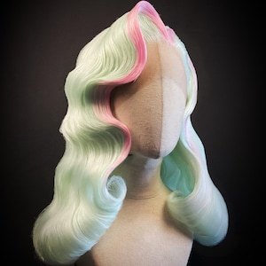 Puede incluir: Peluca de colores pastel con base verde claro y mechas rosas, peinada con ondas voluminosas. La peluca se exhibe sobre una cabeza de maniqu&iacute; sobre un fondo oscuro. La peluca tiene un estilo retro.