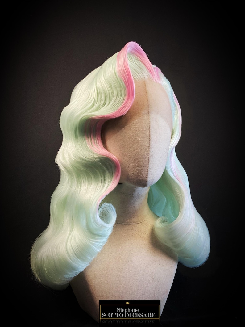 Puede incluir: Peluca de colores pastel con base verde claro y mechas rosas, peinada con ondas voluminosas. La peluca se exhibe sobre una cabeza de maniqu&iacute; sobre un fondo oscuro. La peluca tiene un estilo retro.