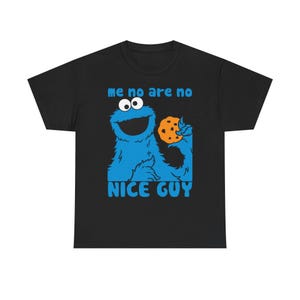 Könnte beinhalten: Schwarzes T-Shirt mit einer blauen Cartoonfigur, die einen Keks hält. Die Figur hat große Augen und ein breites Lächeln. Der Text "me no are no" und "NICE GUY" sind blau gedruckt.