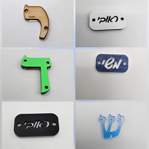 May include: A collection of laser-cut shapes in various colors, including light blue, red, green, and denim blue. The shapes include letters and abstract designs, with some featuring Hebrew text. The items are likely decorative or craft components.