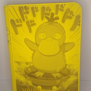 Puede incluir: Carpeta de tarjetas amarilla con un personaje de dibujos animados Psyduck y texto japonés. La carpeta tiene un diseño de estilo cómic y la palabra "vault" en la parte inferior.