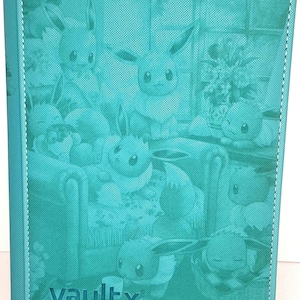 Puede incluir: Carpeta de tarjetas de color turquesa con un diseño en relieve de múltiples personajes de Eevee. La carpeta tiene un borde cosido y la palabra "vaultx" impresa en la esquina inferior izquierda.