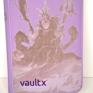 Peut inclure: Un classeur de cartes Vault X lilas avec une illustration marron d'une sorcière marine. Le classeur a une bordure cousue et le logo Vault X dans le coin inférieur. Thème fantastique.